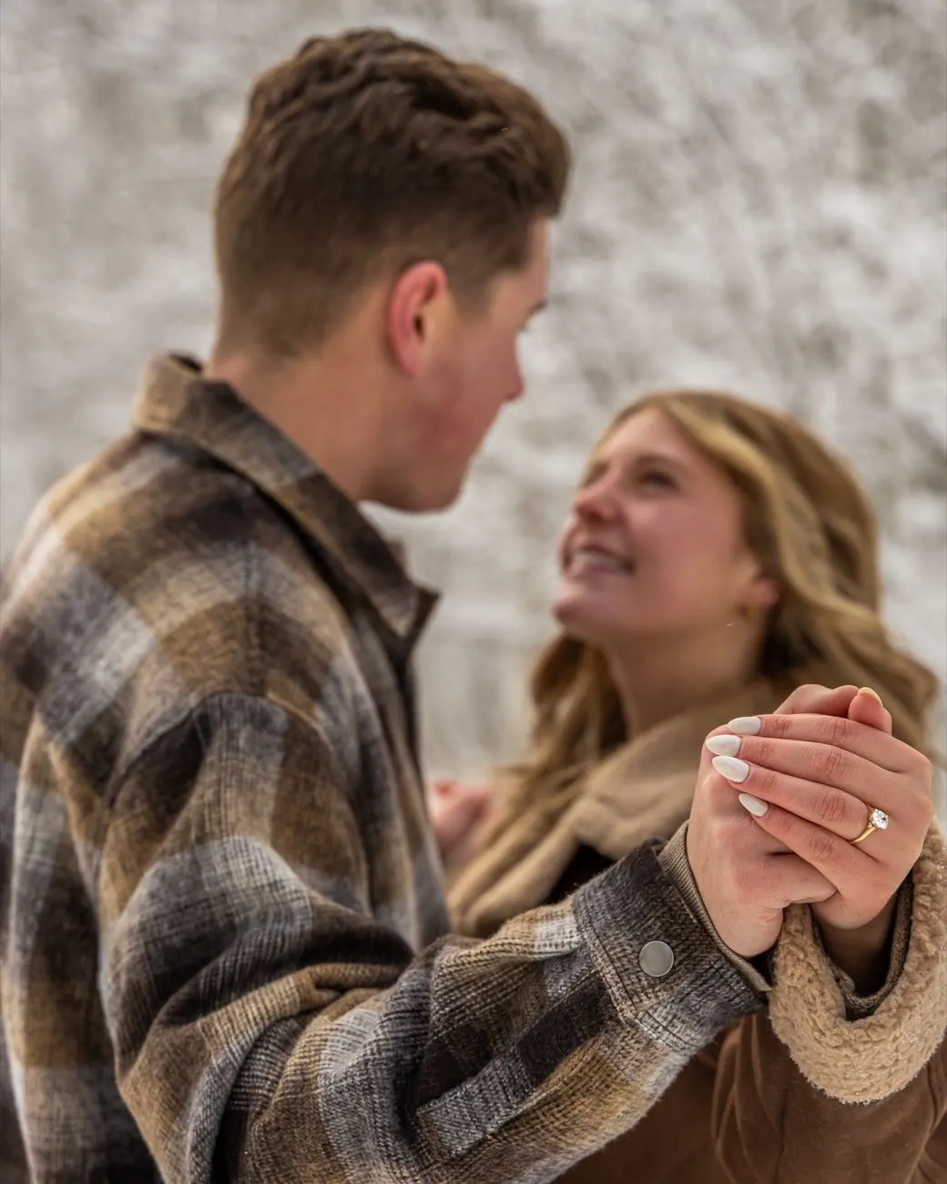 Engaged couple holding hands in the snow, her ring in focus