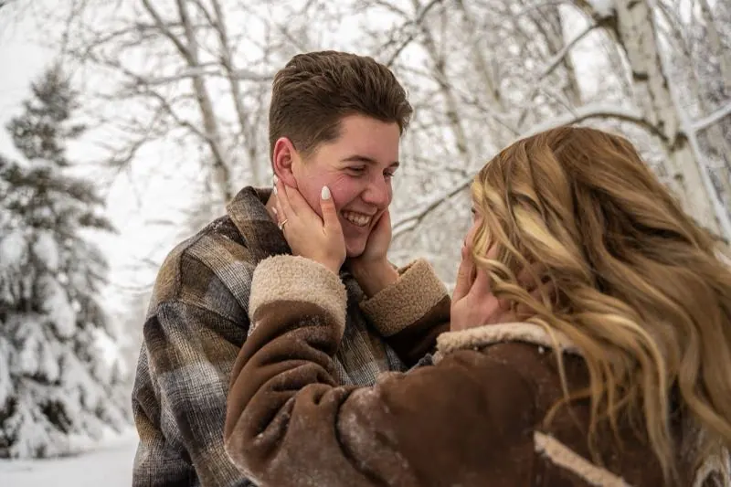 Couple laughing face to face among snowy pines
