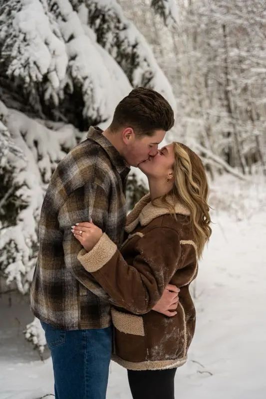 Couple kissing between snow-covered trees